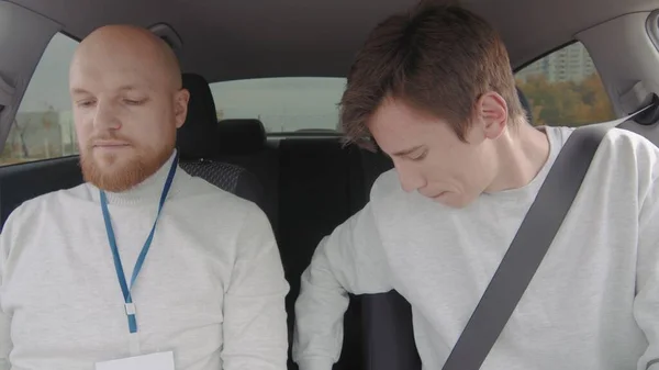 The guy takes a driving test with an instructor. The guy is buckling his seat belt. People drive by car. — Stockfoto