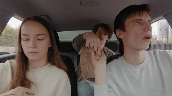 Un pequeño grupo de personas está conduciendo en un coche y comiendo papas fritas. La gente está conduciendo en un coche — Foto de Stock