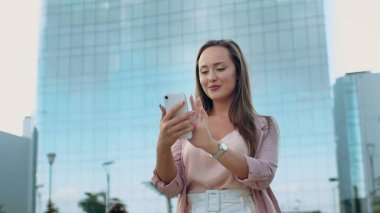 Elinde bir telefonla kameraya doğru yürüyen gülümseyen genç bir kadının yakın çekimi.