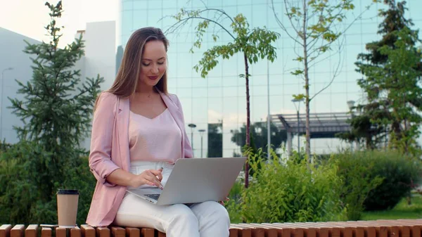 A young woman is sitting at a computer on the street and drinking coffee. Business woman — Stock Photo, Image