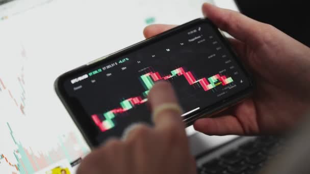 Una chica sostiene un teléfono con un gráfico del mercado de valores en línea que muestra las tendencias bajistas y alcistas de la moneda Bitcoin. En tiempo real. — Vídeo de stock