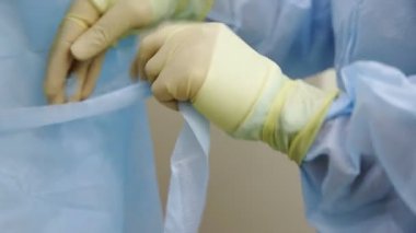 Close-up of professional doctors in uniform, wearing dressing gowns with ties at the back, preparing for surgery. Medicine
