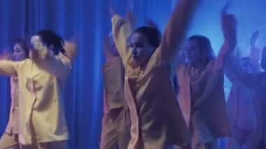 Sarı takım elbiseli mavi ışıklı bir odada dans eden bir grup güzel kız. Dans eder