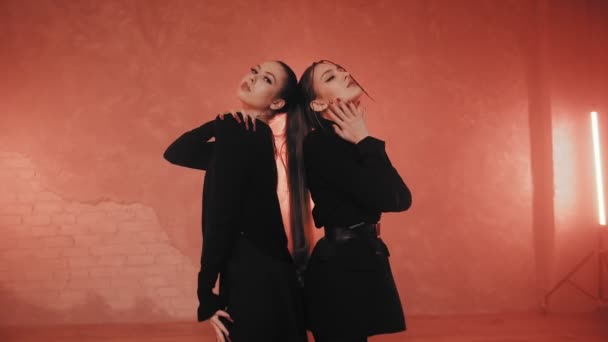 Twee mooie meisjes dansen in een kamer met rood licht in zwart-wit pakken. Dansen — Stockvideo