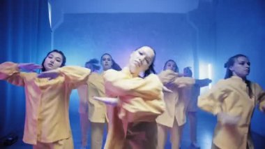 Sarı takım elbiseli mavi ışıklı bir odada dans eden bir grup güzel kız. Dans eder