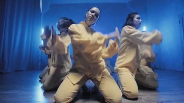 Sarı takım elbiseli mavi ışıklı bir odada dans eden bir grup güzel kız. Dans eder