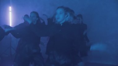 A group of beautiful girls dancing in a room with blue lighting in black suits. Dances