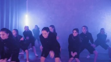 A group of beautiful girls dancing in a room with blue lighting in black suits. The cameraman takes pictures of dancing girls. Dances