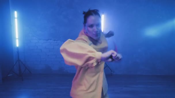 Красива дівчина танцює в приміщенні під синім освітленням в жовтому костюмі. Танці — стокове відео