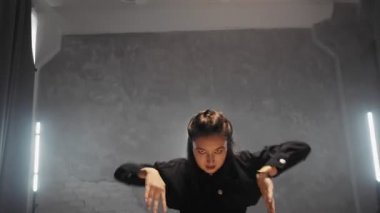A beautiful girl is dancing indoors in a black suit. Dances