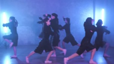 A group of beautiful girls dancing in a room with blue lighting in black suits. Dances