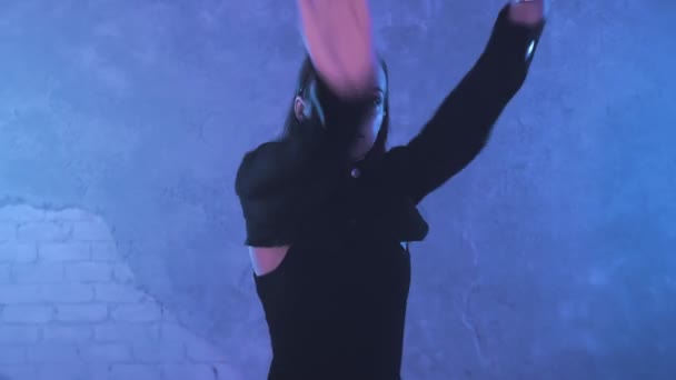 Красива дівчина танцює в приміщенні під синім освітленням в чорному костюмі. Танці — стокове відео