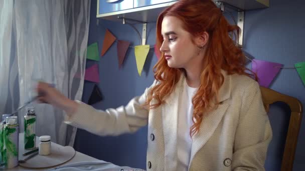 A beautiful red-haired girl drawing with multicolored paints on clothes. Handmade work — Wideo stockowe