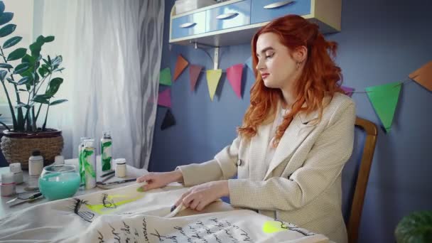 A beautiful red-haired girl, paints with multicolored paints on clothes. Handmade work — Stock video
