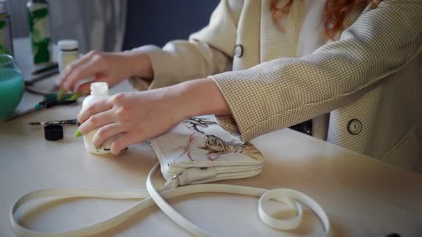 Nahaufnahme eines schönen rothaarigen Mädchens, das mit bunten Farben auf einer Tasche malte. Handarbeit — Stockvideo