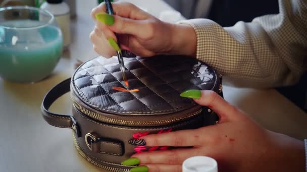 Крупним планом красива руда дівчина малює різнокольоровими фарбами на сумці. Робота ручної роботи — стокове відео