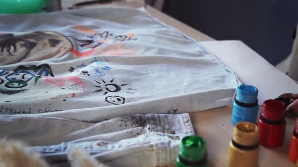 Close-up of a beautiful red-haired girl drawing with multicolored paints on clothes. Handmade work — Vídeo de Stock