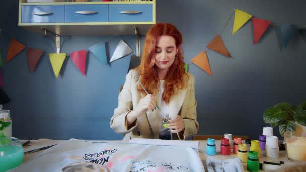 Het algemene plan van een mooie roodharige meisjestekening met veelkleurige verven op kleding. Handgemaakt werk — Stockvideo