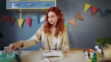 Güzel kızıl saçlı bir kızın genel planı. Çantasına çok renkli boyalar çizmek. Kız videoyu telefonundan izliyor ve çiziyor. El yapımı iş