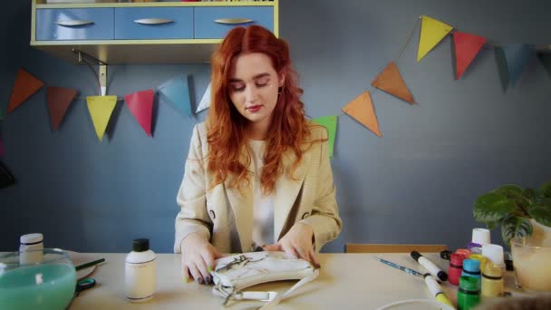 Der Grundriss eines schönen rothaarigen Mädchens, das mit bunten Farben auf einer Tasche zeichnet. Handarbeit — Stockvideo