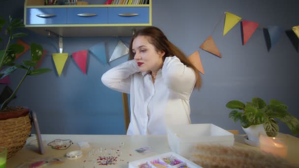 El contorno general de una hermosa chica con una camisa blanca crea una decoración de cuentas. Una chica se prueba una joya de cuentas hecha con sus propias manos. Trabajo hecho a mano — Vídeos de Stock