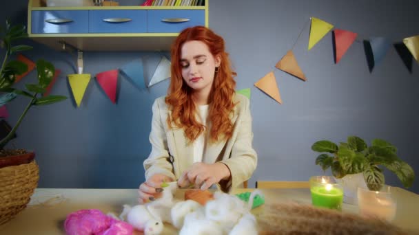 Der allgemeine Plan eines schönen rothaarigen Mädchens, sie rollt Wolle und stellt Spielzeug her. Handarbeit — Stockvideo