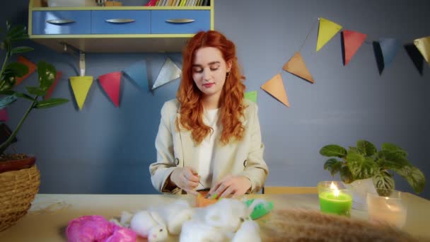 Le plan général d'une belle fille aux cheveux roux, elle roule de la laine et crée des jouets. Travail à la main — Video