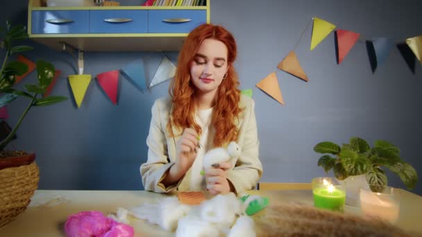 Der allgemeine Plan eines schönen rothaarigen Mädchens, sie rollt Wolle und stellt Spielzeug her. Handarbeit — Stockvideo