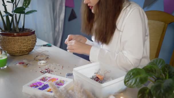 Een close-up van een mooi meisje in een wit shirt zorgt voor een kralendecoratie. Handgemaakt werk — Stockvideo