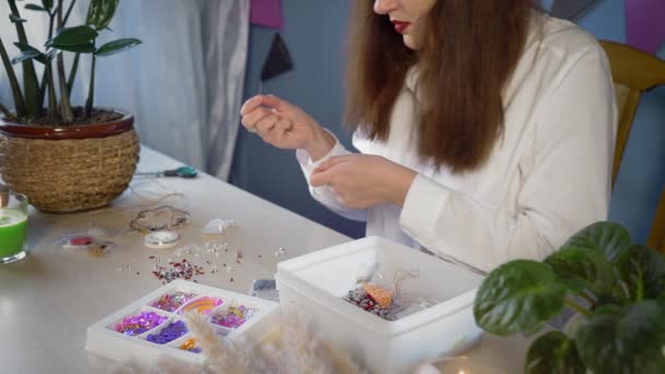 En närbild av en vacker flicka i en vit skjorta skapar en pärla dekoration. Handgjort arbete — Stockvideo