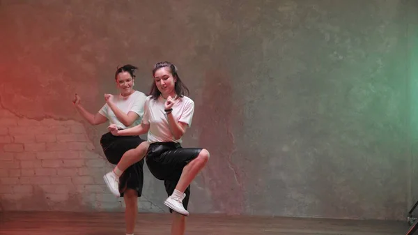 Dos hermosas chicas están bailando en una habitación con iluminación roja y verde y. Bailes — Foto de Stock