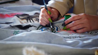 Close-up of a beautiful red-haired girl drawing with multicolored paints on clothes. Handmade work