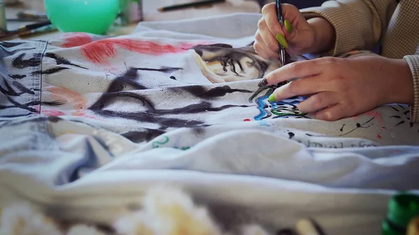 Primer plano de una hermosa chica pelirroja dibujando con pinturas multicolores en la ropa. Trabajo hecho a mano Imágenes de stock libres de derechos