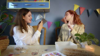 İki güzel kız boncuklardan kendi elleriyle yapılan mücevherleri deniyorlar ve telefonda fotoğraf çekiyorlar. El yapımı iş