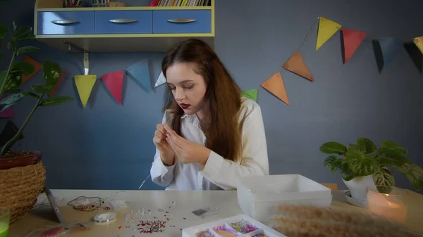 Una hermosa chica con una camisa blanca crea una decoración de cuentas. Trabajo hecho a mano —  Fotos de Stock