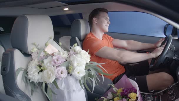 Szczęśliwy facet jeździ samochodem z bukietem kwiatów. Prezenty — Wideo stockowe