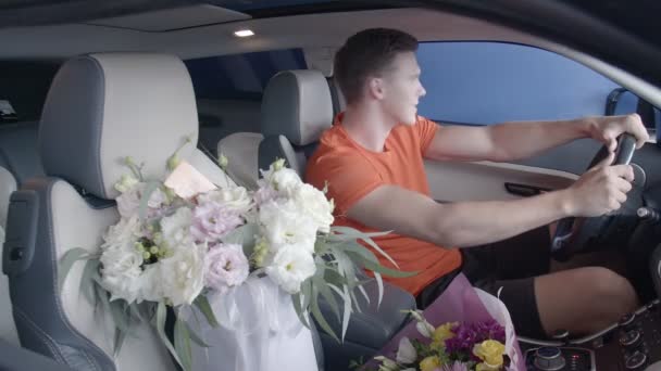 Een gelukkige man rijdt in een auto met een boeket bloemen. Cadeaus — Stockvideo