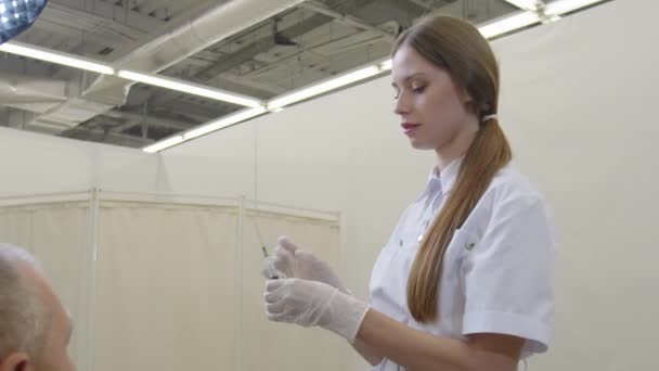 Женщина-врач в маске для лица вакцинирует пациента мужского пола, защищает от коронавируса COVID19 в больничной клинике — стоковое видео