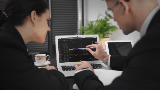 Een zakenman en een vrouw zitten aan een tafel, het analyseren van Bitcoin statistieken op een laptop. Zakenmensen. Close-up — Stockvideo