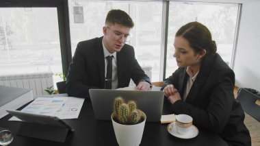 Bir iş adamı ve bir kadın, masada oturup iş meselelerini çözüyorlar. İş adamları