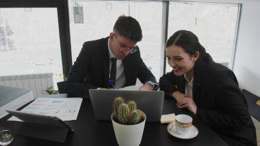 Bir iş adamı ve bir kadın, masada oturup iş meselelerini çözüyorlar. İş adamları