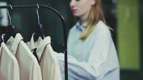 Een leuk meisje kiest kleren in een winkel. Winkelen — Stockvideo