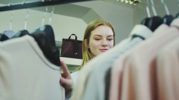 Een leuk meisje kiest kleren in een winkel. Winkelen — Stockvideo