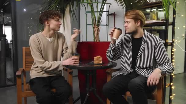 Δύο γκέι άντρες σε ραντεβού κάθονται σε μια καφετέρια, πίνοντας καφέ και γελώντας. ΛΟΑΤ — Αρχείο Βίντεο