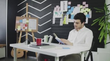 Kafkas görünümlü genç bir adam bir masada oturuyor ve bir kitap okuyor. Genç adam uzaktan çalışıyor.