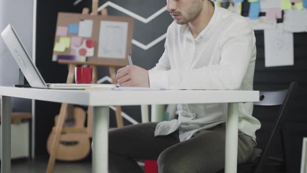 Молодой человек кавказской внешности рисует на графической табличке. Удаленная работа. Фрилансер. Видео в движении — стоковое видео