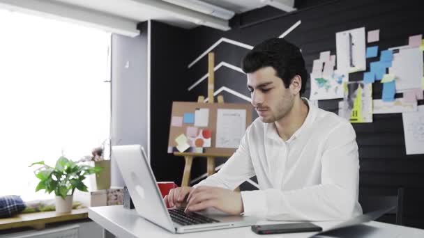En ung mand af kaukasisk udseende sidder ved en computer. Fjernarbejde. Freelance. Video i bevægelse – Stock-video