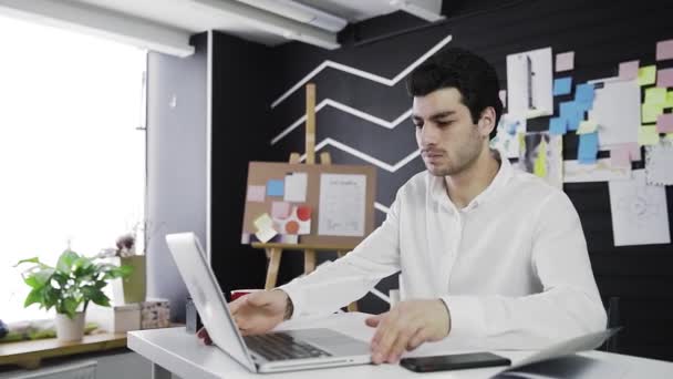 Um jovem de aparência caucasiana liga o computador e começa a trabalhar. Trabalho remoto. Freelance. Vídeo em movimento — Vídeo de Stock