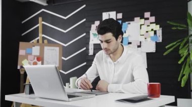 Kafkas görünümlü genç bir adam grafik tablet üzerine resim çizer. Uzaktan kumanda. Serbest çalışıyorum. Hareket halindeki video