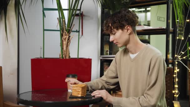 Közelkép egy fickóról, aki egy kávézóban ül. A fickó mézes sütit eszik és kávét iszik egy hangulatos kávézóban. Kávéház — Stock videók